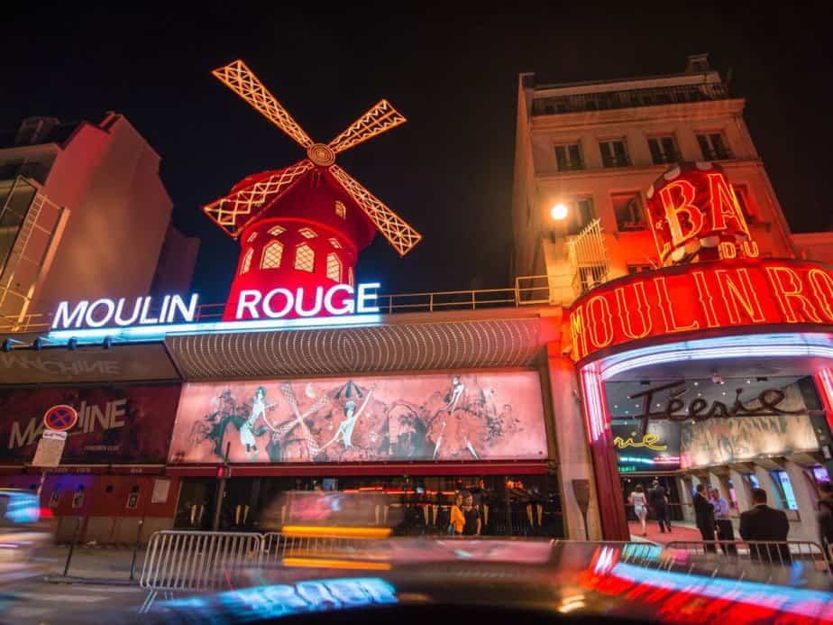 Nighttime view of the iconic Moulin Rouge with its vibrant red windmill, neon signs, and lively entrance, a legendary nightlife spot on any Paris bucket list.