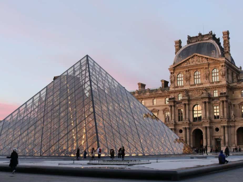 The Louvre Pyramid illuminated at dusk with the historic Louvre Palace in the background, a must-visit landmark for any Paris bucket list.