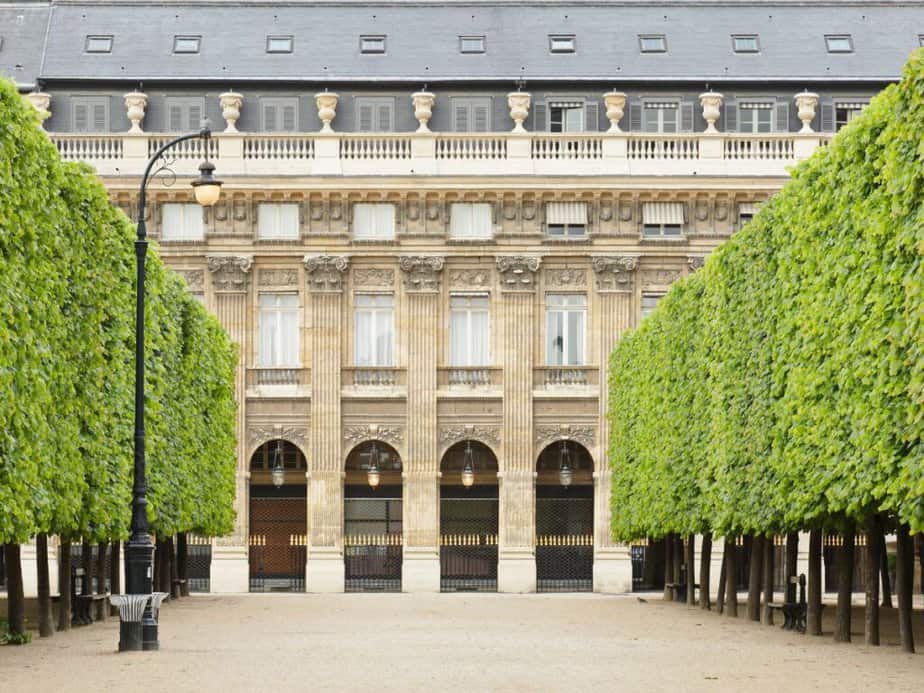 Symmetrical view of the Palais-Royal gardens in Paris, with trimmed trees lining the path leading to a classical French building