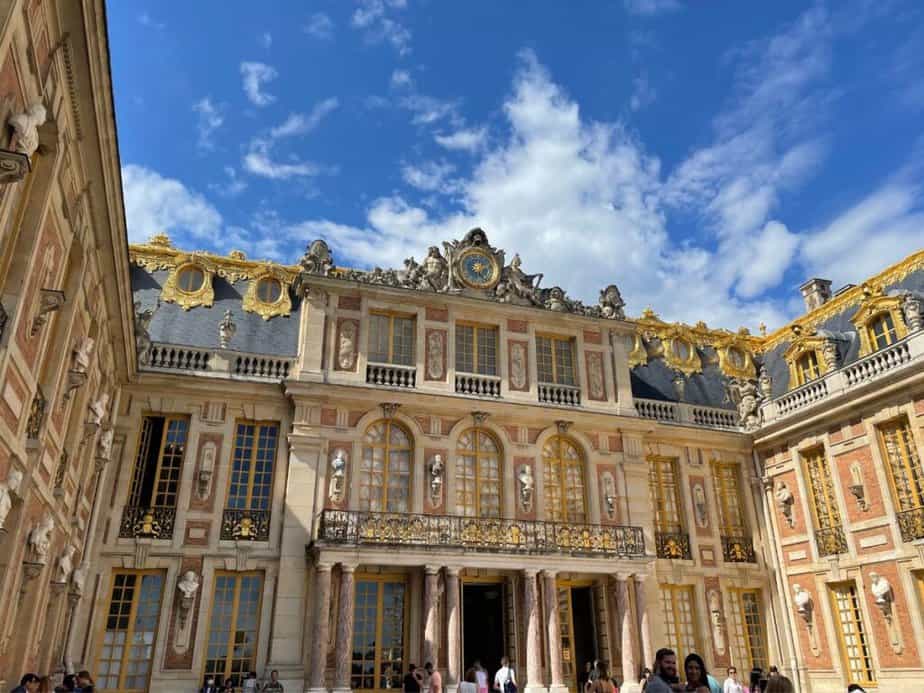 The opulent facade of the Palace of Versailles under a blue sky, adorned with gold trimmings and sculptures, a historical landmark that is a highlight of any Paris bucket list.