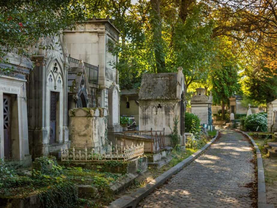 A peaceful cobblestone path meanders through the ancient tombs and autumn-hued trees of Père Lachaise Cemetery in Paris, a reflective destination that's part of the cultural tapestry 