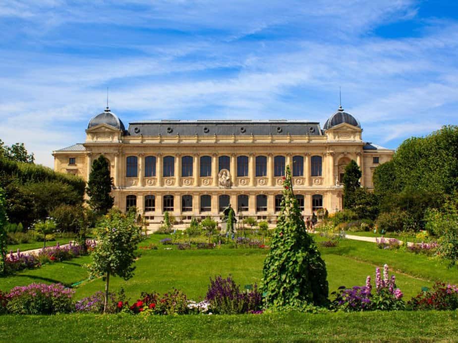 The Jardin des Plantes in Paris, with its lush flowerbeds and vibrant greenery in the foreground, and the elegant Gallery of Evolution building in the background, a tranquil retreat for nature lovers 