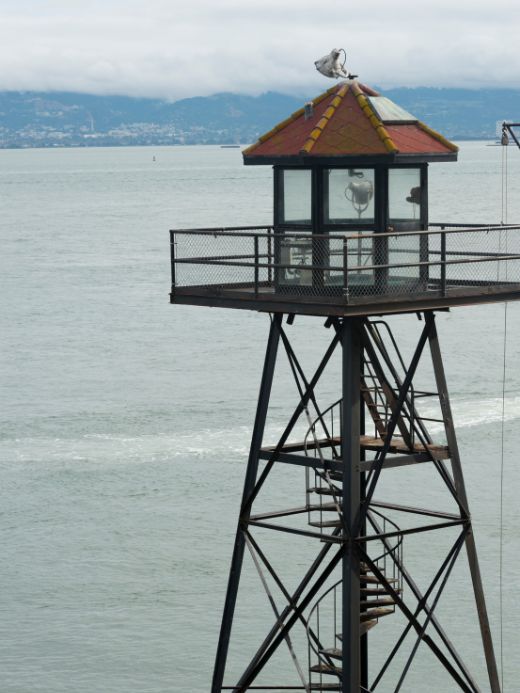 The solitary guard tower of Alcatraz Island standing watch over the San Francisco Bay, with a seagull perched on top, offering a silent testament to the island's history and adding to the debate if the Alcatraz tour is worth it.